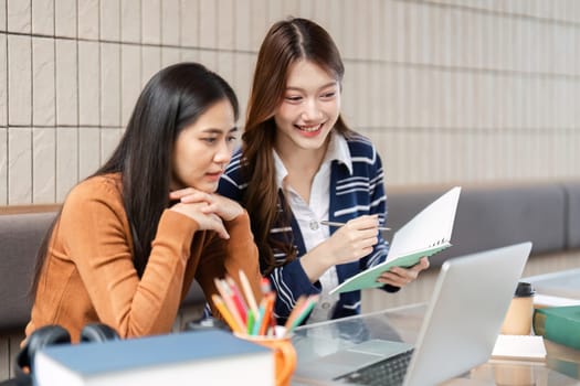 Two friends collaborate on their assignments, using a laptop and notebooks to enhance their learning experience in a warm and inviting study atmosphere.