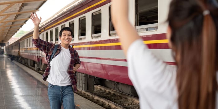 A man waves goodbye to his partner at the train station, embodying excitement and emotion as they begin their journey.