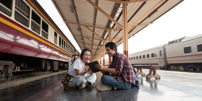 The couple shares joyous moments, exploring travel plans on a tablet, illustrating their excitement and connection as they wait for their train.