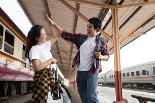 A joyful couple shares a high-five at the train station, excited about their travel plans. Their cheerful demeanor captures the essence of love and adventure.