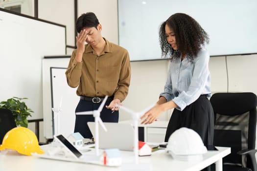 Two professionals engaged in a tense meeting about renewable energy projects, surrounded by models and tools, highlighting sustainable practices in the workplace.