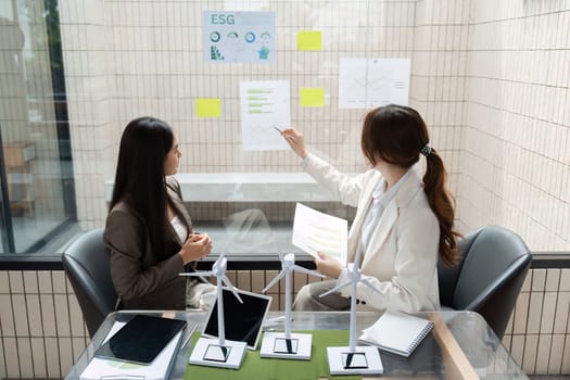 Two women are brainstorming in an office environment, reviewing ESG reports and discussing strategies to enhance sustainable practices in their organization.