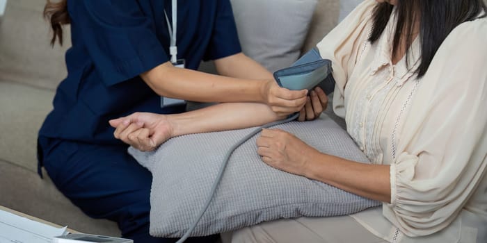 In a cozy home environment, a caregiver skillfully checks the blood pressure of an elderly woman, ensuring ease and comfort during the assessment.