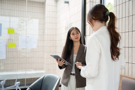 In a modern workspace, a woman presents her ESG findings, while her colleague listens intently, highlighting the importance of collaboration in promoting sustainable initiatives.