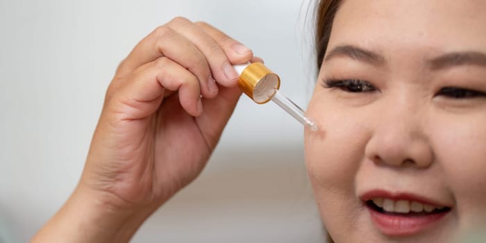 A woman demonstrates her skincare routine, applying a serum with precision to enhance her natural beauty and achieve a glowing skin appearance.