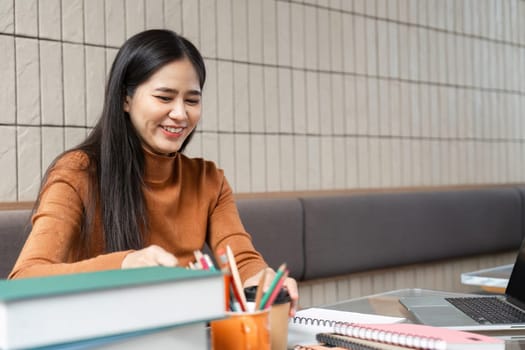 A focused student prepares for a successful study session in a cafe, happily engaging with her notes and laptop while surrounded by school supplies.