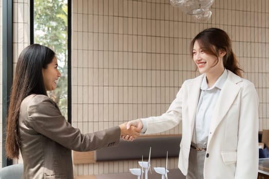 In a bright office setting, two women professionals close a deal with a handshake, fostering commitments to sustainable and renewable energy solutions.