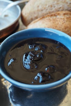 A rich dark chocolate sauce is served in a blue bowl alongside bread.