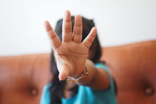A child playfully stopping the camera with a hand gesture indoors.