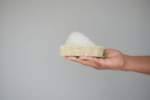 Hand Holding a Foam Soap Sponge Against a Neutral Background.