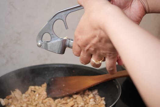 Cooking chicken in a skillet with a garlic press in a home kitchen,