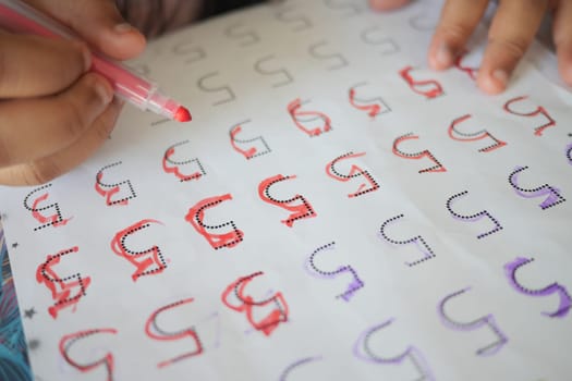 A child practices letter writing using markers on printed sheets.
