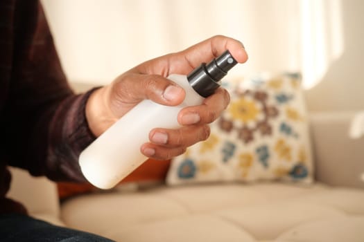 Close-Up of Hand Spraying Cleaner on Upholstered Sofa in Living Room.