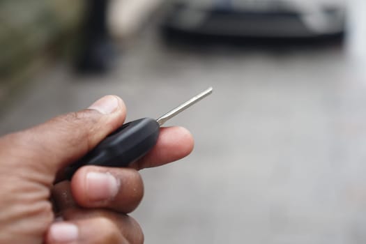 A person is gripping a car key, focused on a nearby vehicle.