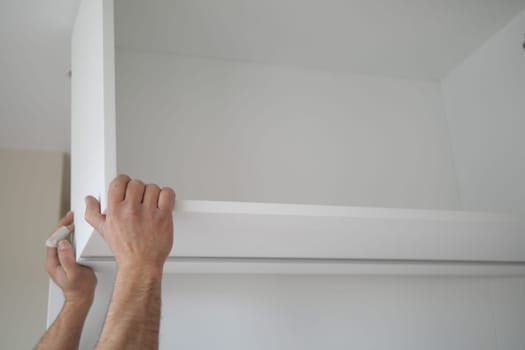 Worker adjusts a white shelf against a light wall in a modern space.