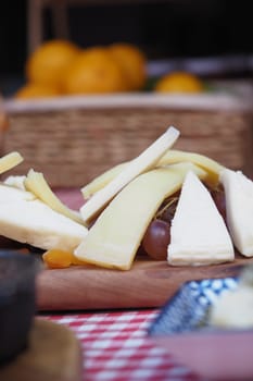 Assorted cheese slices on a wooden board with fresh fruit nearby.