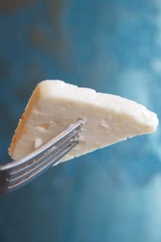 A fork holds a wedge of cheese against a blue textured backdrop.
