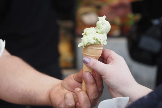 A person is handing an ice cream cone to another individual in a lively setting.