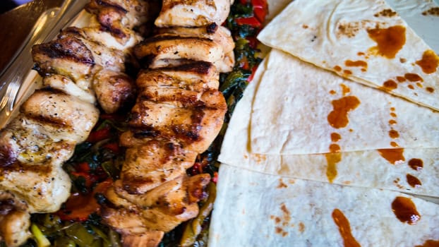 Grilled chicken skewers served with vegetables and tortillas on plate.