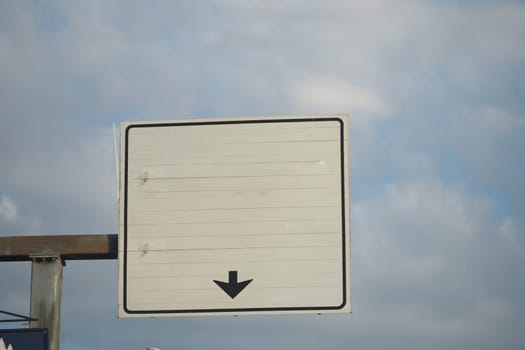 Blank traffic sign with downward arrow against a cloudy background.