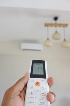 Hand holds a remote control while aiming at an air conditioner.