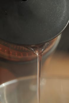 Warm water is being poured from a kettle into a clear glass teapot.