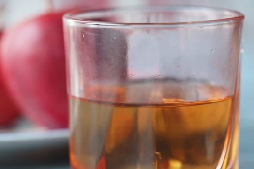 Golden apple juice is poured into a clear glass beside fresh red apples.