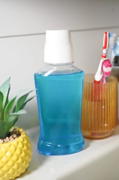 Bright blue mouthwash bottle next to toothbrushes in a bathroom.