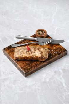 Juicy grilled ribs on a rustic wooden board, with a small bowl of mixed spices. A knife and fork are elegantly placed beside the meat, enhancing the appetizing presentation.