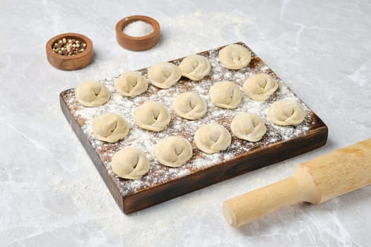 Handmade beef dumplings on a floured wooden board with a rolling pin nearby
