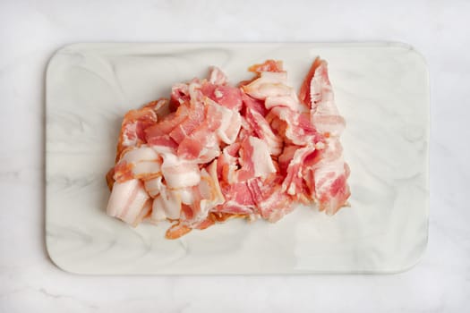 Slices of freshly chopped pork bacon on a marble cutting board, showcasing their pink and white marbling. The preparation suggests cooking or meal planning.