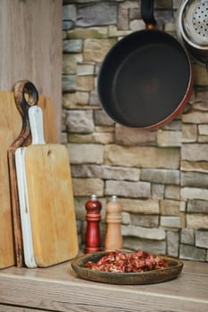 A cozy kitchen features wooden cutting boards and a rustic stone wall. Ingredients await preparation in a bowl, while a frying pan hangs above, highlighting the culinary atmosphere.