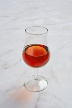 A delicate glass filled with a smooth, amber-colored brandy on a light marble table. The drink's rich hue reflects the soft light, inviting a closer look at its clarity.
