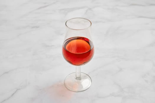 A crystal-clear glass filled with a rich brandy on a smooth marble surface. Natural light reflects off the glass, enhancing its color and creating an inviting ambiance.