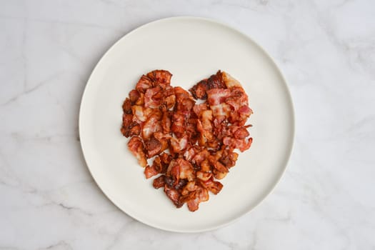 Crispy bacon pieces are creatively arranged on a white plate to form a heart shape, presenting an artistic expression of affection for breakfast delights.