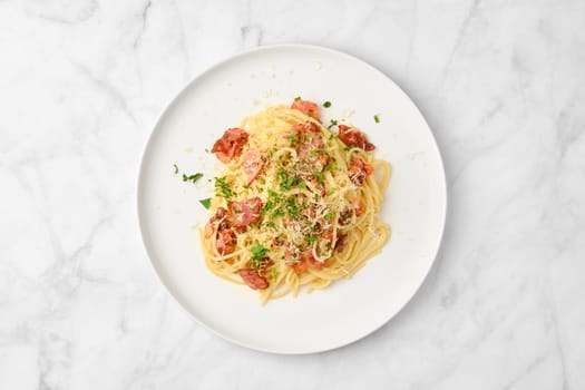 A bowl of spaghetti topped with crispy bacon and grated cheese sits on a clean, white plate. Fresh parsley garnishes the dish, creating an appealing presentation ready to be enjoyed.