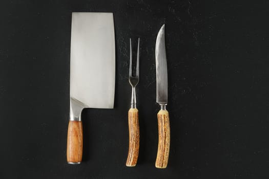 Three essential kitchen tools on a dark background, featuring a cleaver, carving fork, and a paring knife. These tools are perfect for slicing, chopping, and serving food.