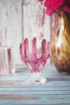 A pink glass vase holds vibrant flowers while resting on a wooden surface.
