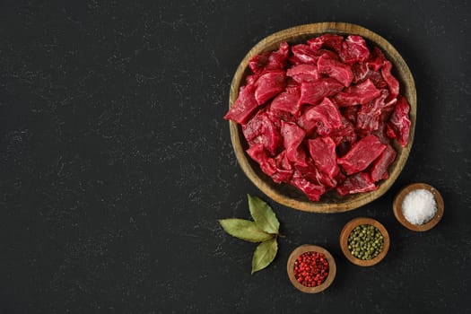 A wooden bowl with freshly diced beef pieces alongside spices in small bowls