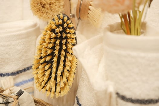 A natural cleaning brush hangs among towels and decorative items in a bathroom.