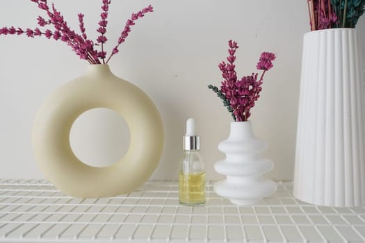 Two unique vases with dried flowers and an essential oil bottle display beauty.