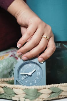 A hand reaches out to set a clock nestled on a bedside table.