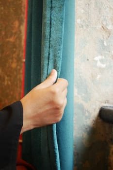 A hand pulls a soft blue curtain in a charming, textured room.