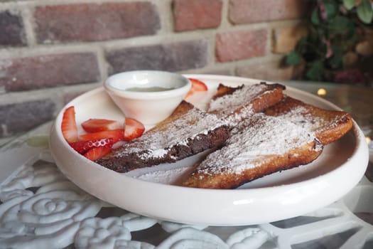 A plate of French toast garnished with powdered sugar and strawberries.