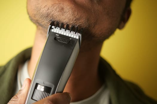 Individual trims facial hair using an electric trimmer indoors.