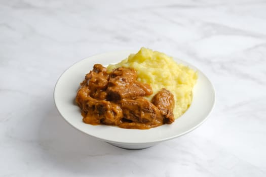 Plate with beef goulash with mashed potato in a deep plate on marble background