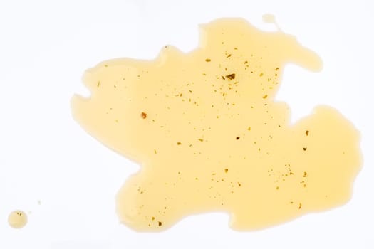 Olive oil with herbs is spread across a white surface, featuring dark specks that add visual interest.