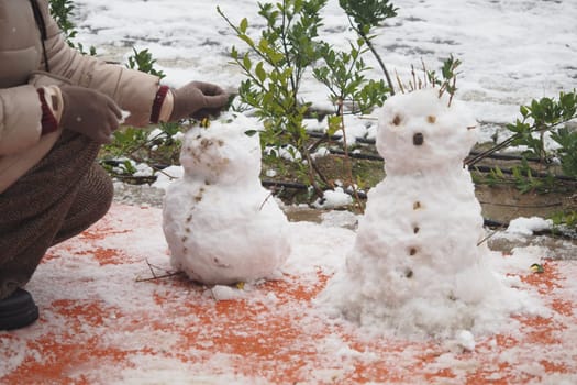Children build two cheerful snowmen with decorative features outdoors.