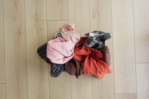 A woven basket of neatly arranged clothes rests on a wooden floor.