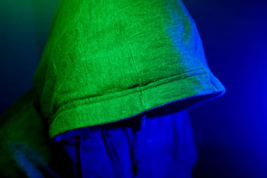 A figure in a hooded jacket is illuminated by colorful lights at night.